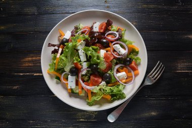 Taze salatalık, kiraz domates, tatlı biber, marul, kırmızı soğan, zeytin ve zeytin yağı ile koyu ahşap rustik arka planda Yunan salatası. Sağlıklı gıda konsepti