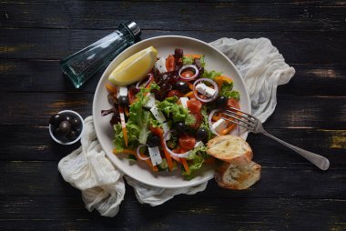 Taze salatalık, kiraz domates, tatlı biber, marul, kırmızı soğan, zeytin ve zeytin yağı ile koyu ahşap rustik arka planda Yunan salatası. Sağlıklı gıda konsepti