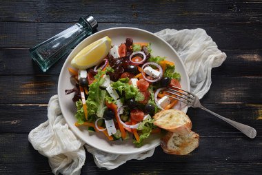 Taze salatalık, kiraz domates, tatlı biber, marul, kırmızı soğan, zeytin ve zeytin yağı ile koyu ahşap rustik arka planda Yunan salatası. Sağlıklı gıda konsepti