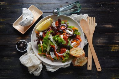 Taze salatalık, kiraz domates, tatlı biber, marul, kırmızı soğan, zeytin ve zeytin yağı ile koyu ahşap rustik arka planda Yunan salatası. Sağlıklı gıda konsepti