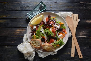 Taze salatalık, kiraz domates, tatlı biber, marul, kırmızı soğan, zeytin ve zeytin yağı ile koyu ahşap rustik arka planda Yunan salatası. Sağlıklı gıda konsepti