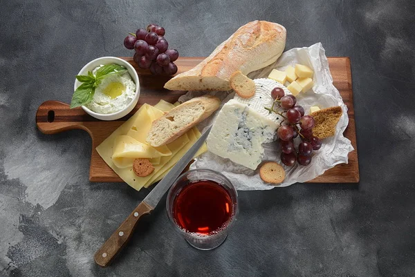 Cheese platter with assorted cheese, grapes, snacks on dark background. Italian, French cheese starter