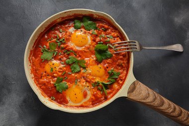 Shakshuka , orta doğu geleneksel ev yapımı kahvaltı- kızarmış yumurta, soğan, biber, domates ve maydanoz koyu bir arka plan üzerinde bir tavada 