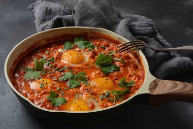 Shakshuka , orta doğu geleneksel ev yapımı kahvaltı- kızarmış yumurta, soğan, biber, domates ve maydanoz koyu bir arka plan üzerinde bir tavada 