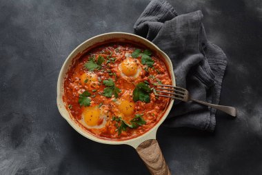 Shakshuka , orta doğu geleneksel ev yapımı kahvaltı- kızarmış yumurta, soğan, biber, domates ve maydanoz koyu bir arka plan üzerinde bir tavada 