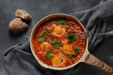 Shakshuka , orta doğu geleneksel ev yapımı kahvaltı- kızarmış yumurta, soğan, biber, domates ve maydanoz koyu bir arka plan üzerinde bir tavada 