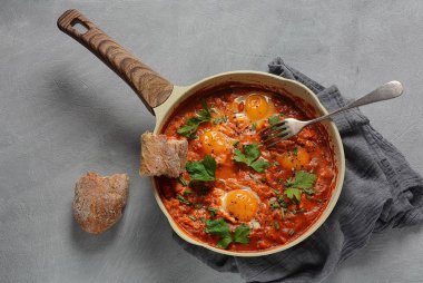 Shakshuka , orta doğu geleneksel ev yapımı kahvaltı- kızarmış yumurta, soğan, biber, domates ve maydanoz koyu bir arka plan üzerinde bir tavada 