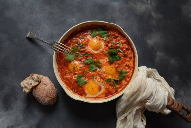 Shakshuka , orta doğu geleneksel ev yapımı kahvaltı- kızarmış yumurta, soğan, biber, domates ve maydanoz koyu bir arka plan üzerinde bir tavada 