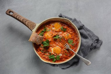 Shakshuka , orta doğu geleneksel ev yapımı kahvaltı- kızarmış yumurta, soğan, biber, domates ve maydanoz koyu bir arka plan üzerinde bir tavada 