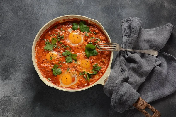 Shakshuka , orta doğu geleneksel ev yapımı kahvaltı- kızarmış yumurta, soğan, biber, domates ve maydanoz koyu bir arka plan üzerinde bir tavada 