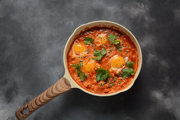 Shakshuka , orta doğu geleneksel ev yapımı kahvaltı- kızarmış yumurta, soğan, biber, domates ve maydanoz koyu bir arka plan üzerinde bir tavada 
