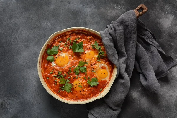 Shakshuka , orta doğu geleneksel ev yapımı kahvaltı- kızarmış yumurta, soğan, biber, domates ve maydanoz koyu bir arka plan üzerinde bir tavada 