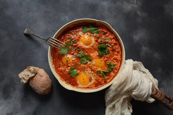 Shakshuka , orta doğu geleneksel ev yapımı kahvaltı- kızarmış yumurta, soğan, biber, domates ve maydanoz koyu bir arka plan üzerinde bir tavada 