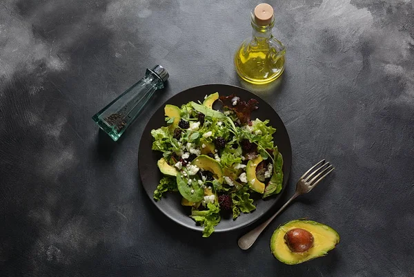 Avocado salad with lettuce, blackberry, blue cheese, olive oil and arugula on a plate. Healthy vegan food concept