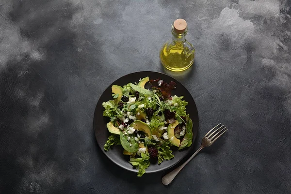 Avocado salad with lettuce, blackberry, blue cheese, olive oil and arugula on a plate. Healthy vegan food concept
