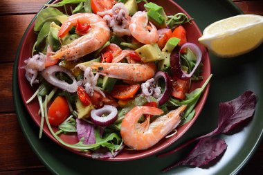 Karides, avokado, kiraz domates, kırmızı acı biber, kırmızı soğan, arugula, pancar yaprakları, rukola.balsamik sos bir tabak ta bir ahşap arka plan sağlıklı deniz gıda kavramı ile deniz gıda salatası
