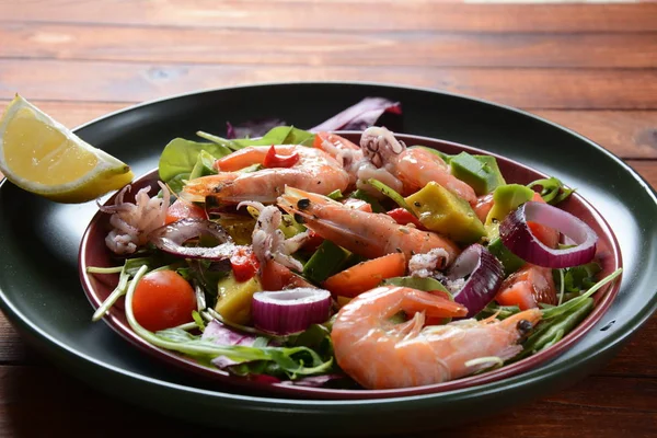 Sea food salad with shrimps, avocado, cherry tomatoes, red hot chilly pepper, red onion, arugula, beet leaves,rukola.balsamic sauce in a plate on a wood background Healthy sea food concept