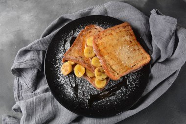 Kızarmış plantains ile Fransız tost, akçaağaç şurubu damlama, siyah bir tabak tabaktabaktabak tabaktabak tabaktabak tabaktabak tabaktabak tabaktabak tabaktabak şeker tozu. Fransız tatlı konsepti. Tatlı ve lezzetli kahvaltı 