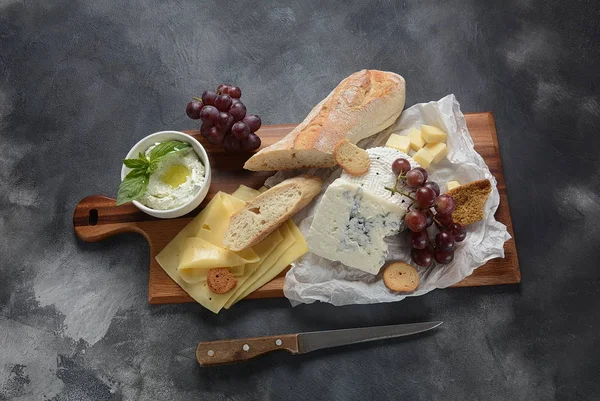 Cheese platter with assorted cheeses, grapes, snacks on dark background. Italian, French cheese starter