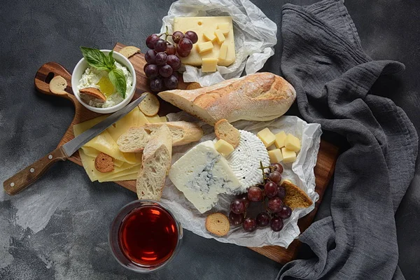 Cheese platter with assorted cheeses, grapes, snacks on dark background. Italian, French cheese starter