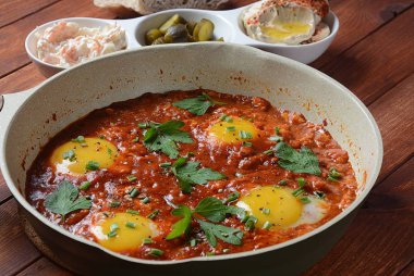Shakshuka , orta doğu geleneksel ev yapımı kahvaltı- kızarmış yumurta, soğan, biber, domates ve maydanoz bir tavada ahşap bir arka plan humus ile servis