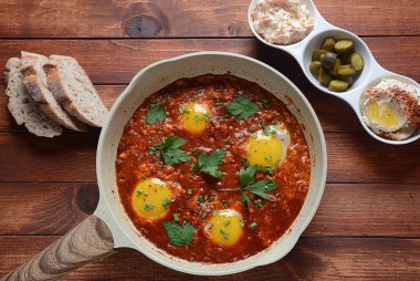 Shakshuka , orta doğu geleneksel ev yapımı kahvaltı- kızarmış yumurta, soğan, biber, domates ve maydanoz bir tavada ahşap bir arka plan humus ile servis