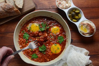 Shakshuka , orta doğu geleneksel ev yapımı kahvaltı- kızarmış yumurta, soğan, biber, domates ve maydanoz bir tavada ahşap bir arka plan humus ile servis