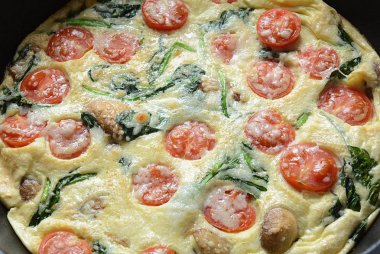Frittata yumurta, mantar, kiraz domates ve ıspanak yapılan bir tavada servis edilir. İtalyan mutfağı.