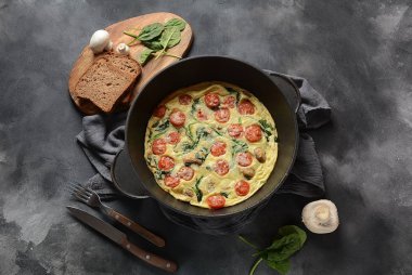 Frittata yumurta, mantar, kiraz domates ve ıspanak yapılan bir tavada servis edilir. İtalyan mutfağı.