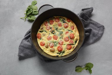 Frittata yumurta, mantar, kiraz domates ve ıspanak yapılan bir tavada servis edilir. İtalyan mutfağı.
