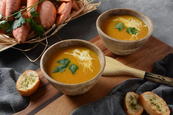 Sweet potato and carrot soup served with sour cream in wooden bowl. Orange vegetable soup concept. Vegan food