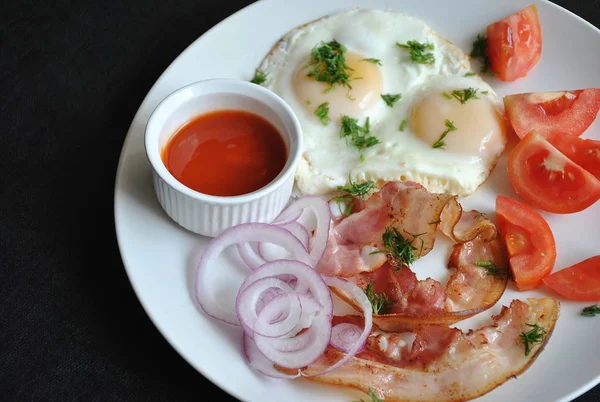 黒い背景の白い皿の上にトマト 赤玉ねぎ ベーコンと目玉焼き おいしい自家製朝食 — ストック写真