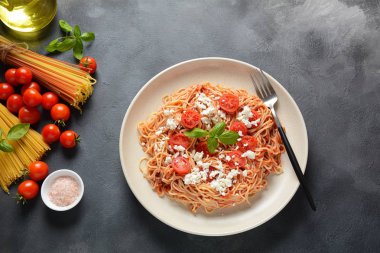 Klasik Italyan spagetti makarna ile domates sosu, mozzarella, kiraz domates ve fesleğen plaka üzerinde koyu masa