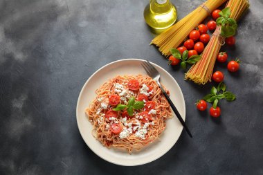 Klasik Italyan spagetti makarna ile domates sosu, mozzarella, kiraz domates ve fesleğen plaka üzerinde koyu masa