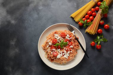 Klasik Italyan spagetti makarna ile domates sosu, mozzarella, kiraz domates ve fesleğen plaka üzerinde koyu masa