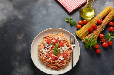 Klasik Italyan spagetti makarna ile domates sosu, mozzarella, kiraz domates ve fesleğen plaka üzerinde koyu masa