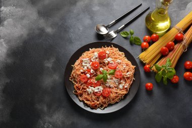 Klasik Italyan spagetti makarna ile domates sosu, mozzarella, kiraz domates ve fesleğen plaka üzerinde koyu masa