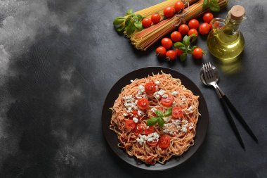 Klasik Italyan spagetti makarna ile domates sosu, mozzarella, kiraz domates ve fesleğen plaka üzerinde koyu masa