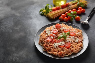 Klasik Italyan spagetti makarna ile domates sosu, mozzarella, kiraz domates ve fesleğen plaka üzerinde koyu masa