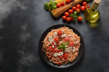 Klasik Italyan spagetti makarna ile domates sosu, mozzarella, kiraz domates ve fesleğen plaka üzerinde koyu masa