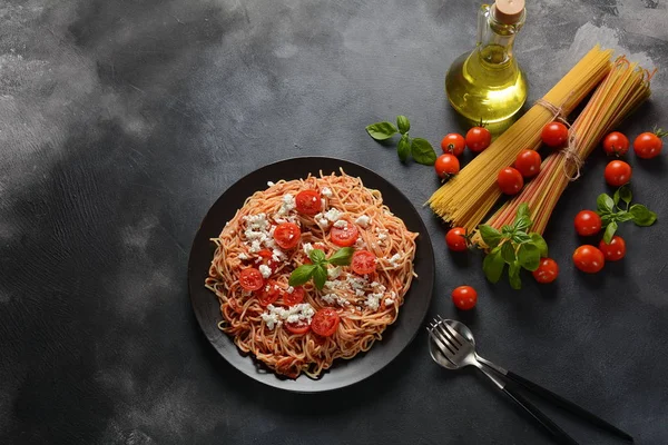 Klasik Italyan spagetti makarna ile domates sosu, mozzarella, kiraz domates ve fesleğen plaka üzerinde koyu masa