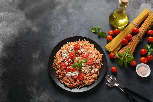 Klasik Italyan spagetti makarna ile domates sosu, mozzarella, kiraz domates ve fesleğen plaka üzerinde koyu masa