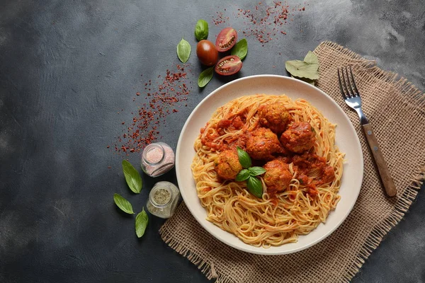 Koyu arka planda beyaz bir plaka üzerinde köfte ve domates sosu ile makarna spagetti