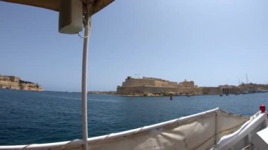 Güçlü Malta forts güzel bir manzara ile kıyıdan yelkenli yat. Deniz kenarında, Akdeniz'de yüzen beyaz burunlu yat. Güneşli hava. Yat güvertesi üzerinden deniz manzarası. Mavi gökyüzü ve turkuaz su. Malta kıyı şeridi