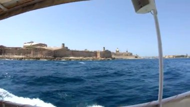 Yat güçlü Malta forts güzel bir manzara ile deniz kenarı boyunca yüzen. Yat güvertesi üzerinden deniz manzarası. Mavi gökyüzü ve turkuaz su. Köpük lü dalgalar. Malta, sahil şeridi.