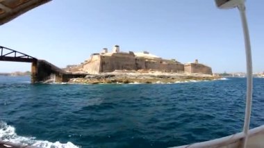 Yat güçlü Malta forts güzel bir manzara ile deniz kenarı boyunca yüzen. Yat güvertesi üzerinden deniz manzarası. Mavi gökyüzü ve turkuaz su. Köpük lü dalgalar. Malta, sahil şeridi.