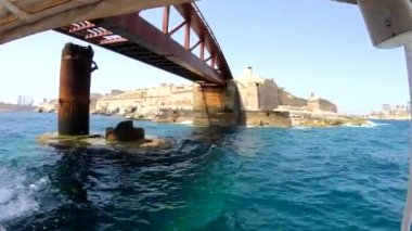 Yat güçlü Malta forts güzel bir manzara ile deniz kenarı boyunca yüzen. Yat güvertesi üzerinden deniz manzarası. Mavi gökyüzü ve turkuaz su. Köpük lü dalgalar. Malta, sahil şeridi.