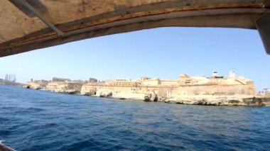 Yat güçlü Malta forts güzel bir manzara ile deniz kenarı boyunca yüzen. Yat güvertesi üzerinden deniz manzarası. Mavi gökyüzü ve turkuaz su. Köpük lü dalgalar. Malta, sahil şeridi.