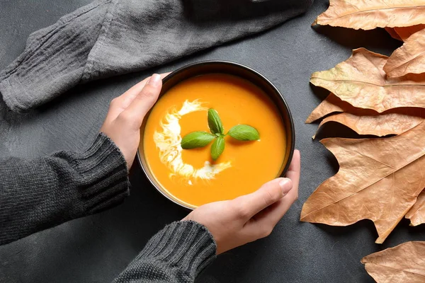 Bowl of pumpkin and carrot cream soup in hands. Autumn hot vegan soup concept