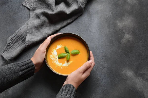 Bowl of pumpkin and carrot cream soup in hands. Autumn hot vegan soup concept